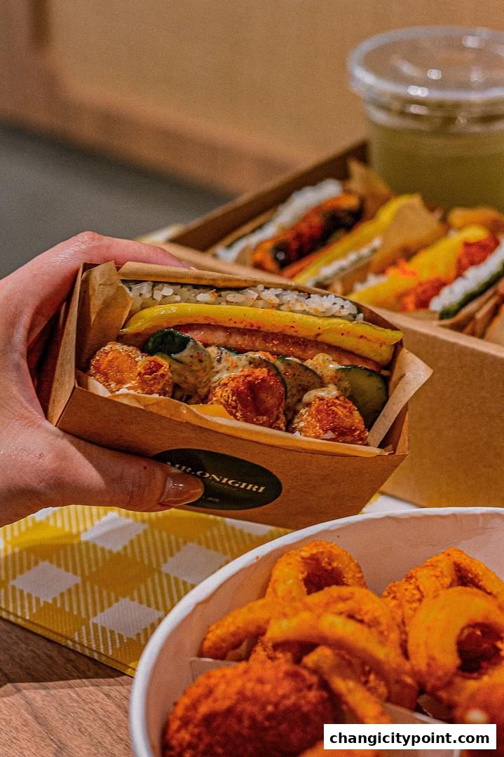A hand holds a delicious onigiri sandwich with fried chicken and vegetables.