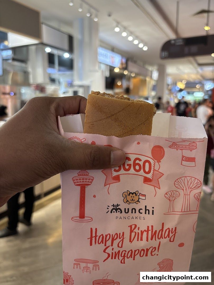 A hand holds a pancake from Munchi Pancakes in a festive Singapore-themed bag.
