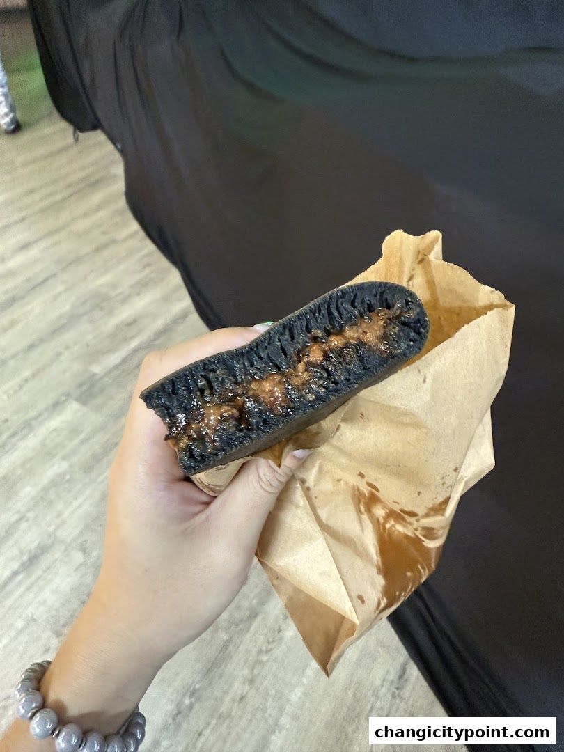 A hand holds a dark-colored pancake filled with a sweet, gooey filling.