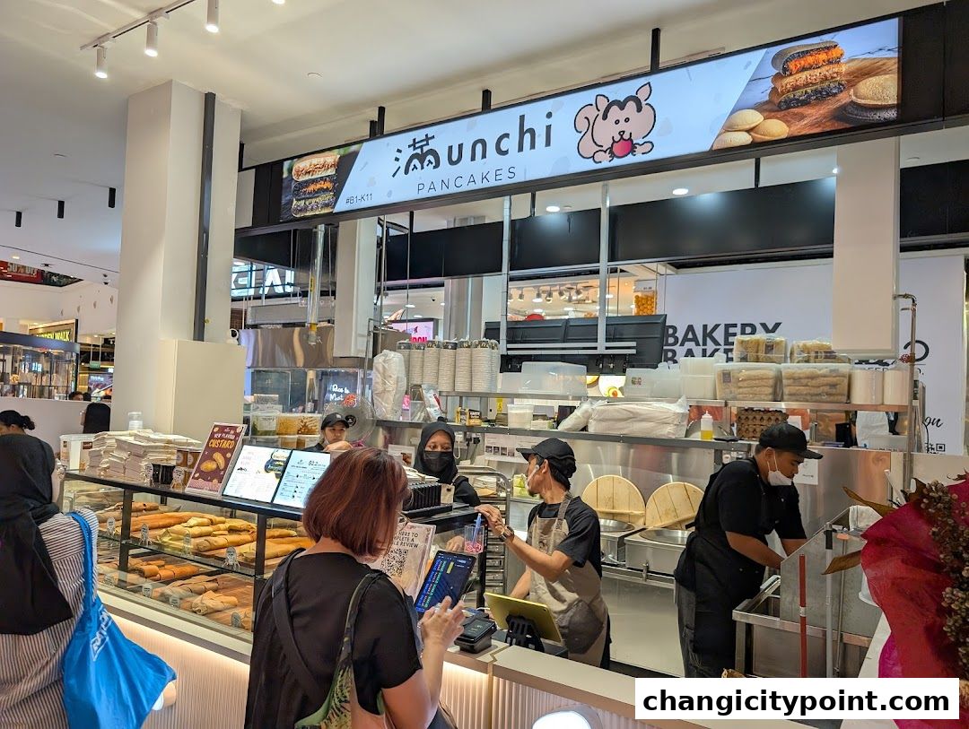 A view of the Munchi Pancakes shop counter with staff serving customers and displaying various pancake items.