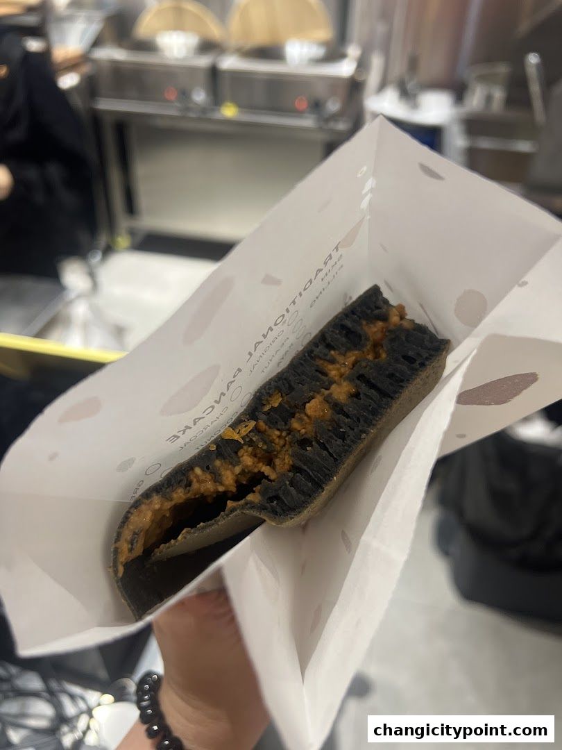 A close-up of a charcoal pancake filled with peanut butter, held in a paper bag.