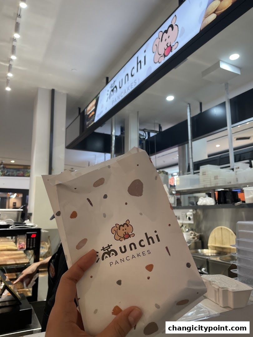 A hand holds a branded paper bag from Munchi Pancakes in front of the shop.