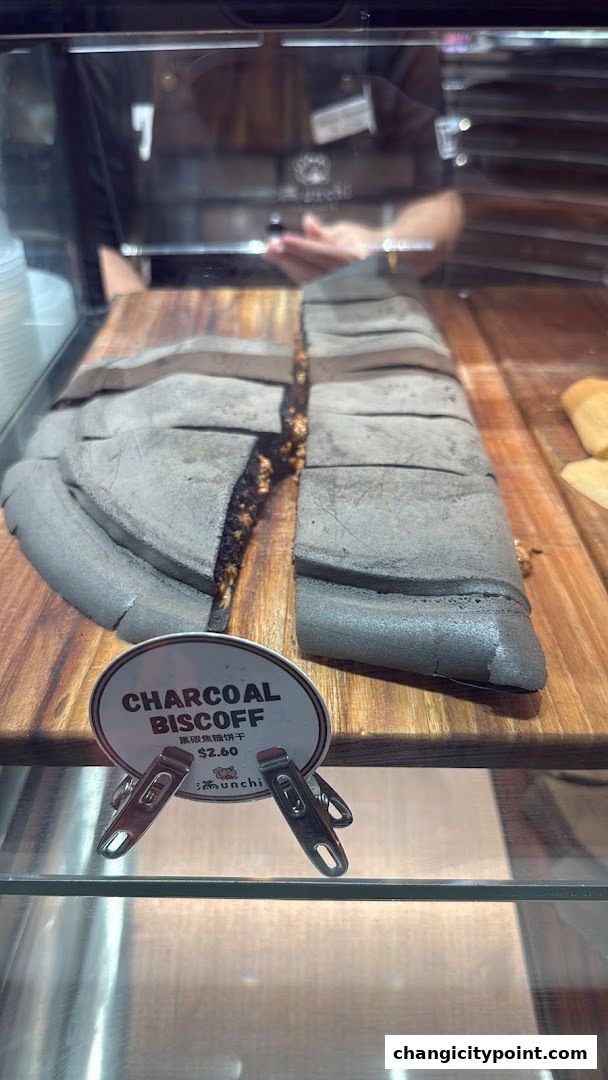 A sliced charcoal biscoff cookie on a wooden board in a display case.