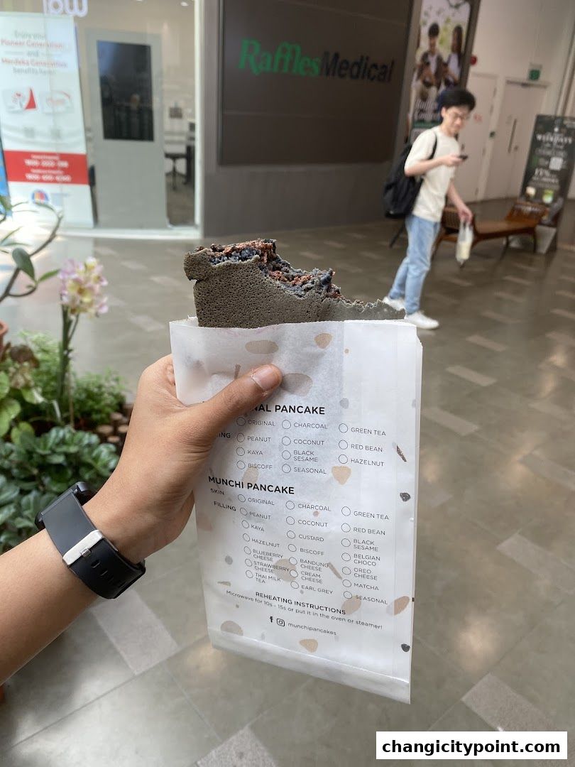 A hand holds a partially eaten charcoal pancake from Munchi Pancakes.