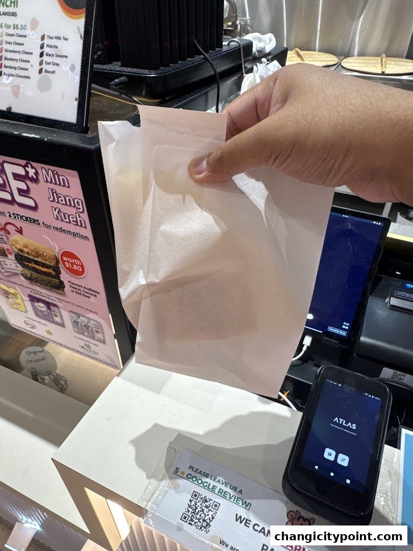 A hand holds a paper bag in front of a counter with a menu and payment devices.