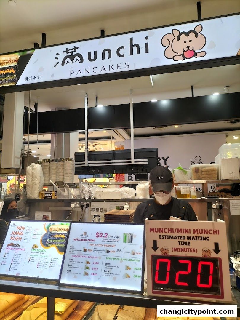 A shop front for Munchi Pancakes with menus and a digital waiting time display.