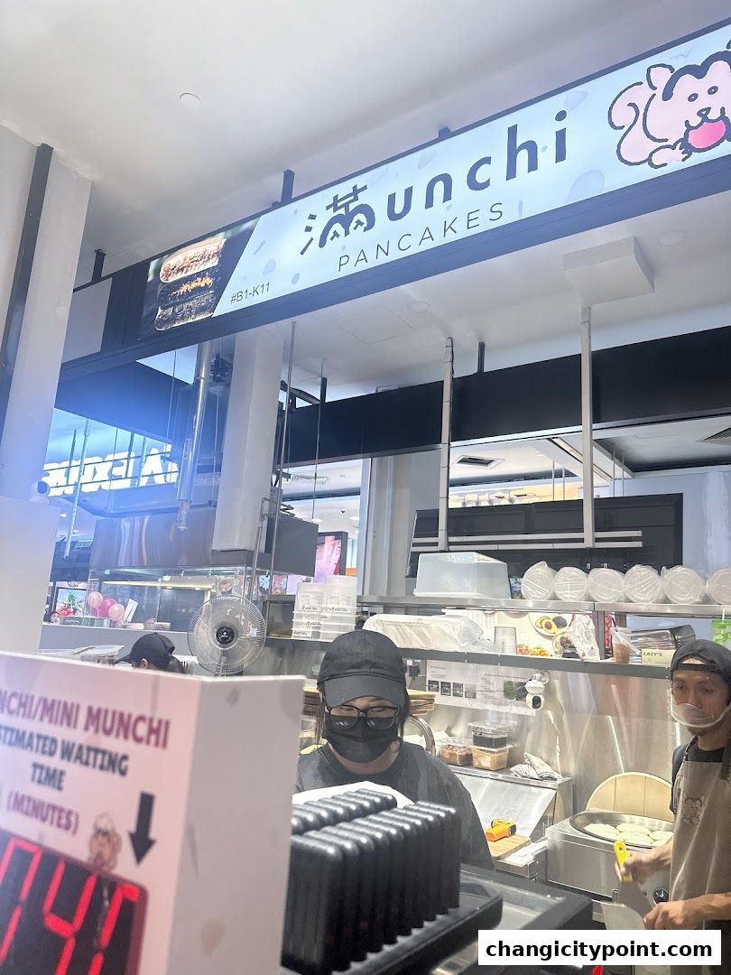 The entrance of Munchi Pancakes shop with staff preparing food and a waiting time display.