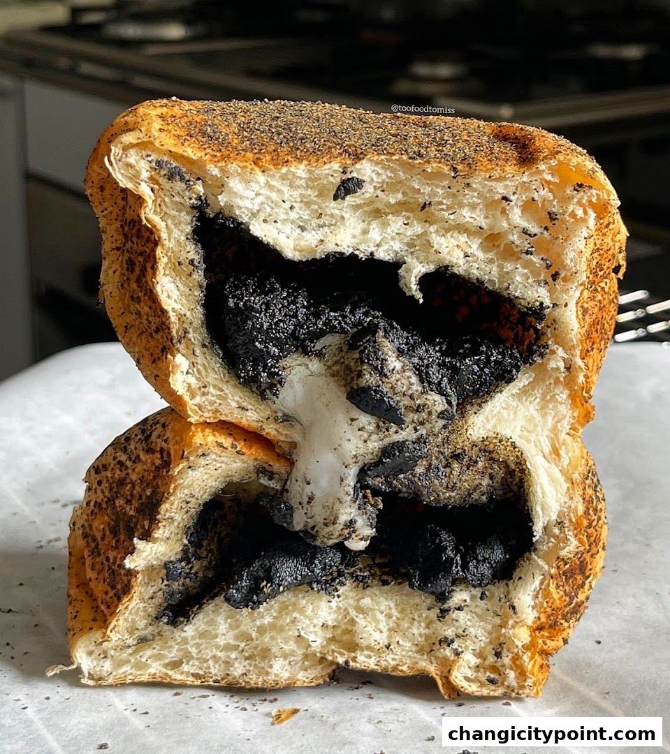 A close-up shot of a halved bread roll filled with black sesame paste and white cream.