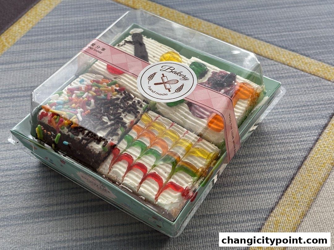 A clear plastic box filled with assorted colorful pastries and cakes.