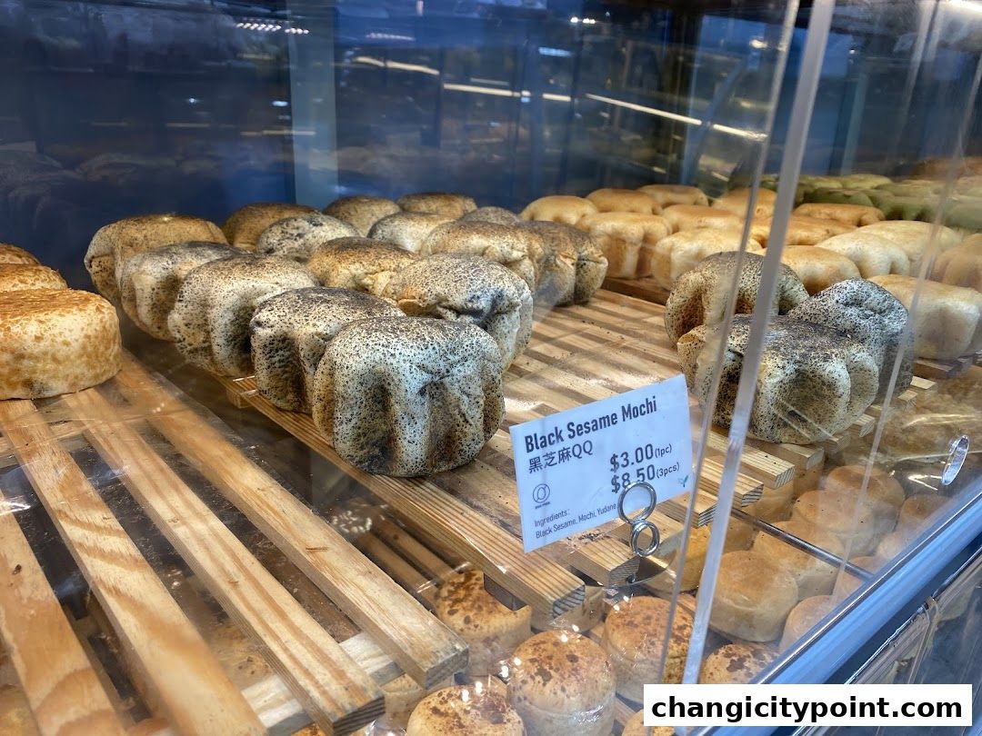 A display of freshly baked black sesame mochi and other pastries in a bakery.