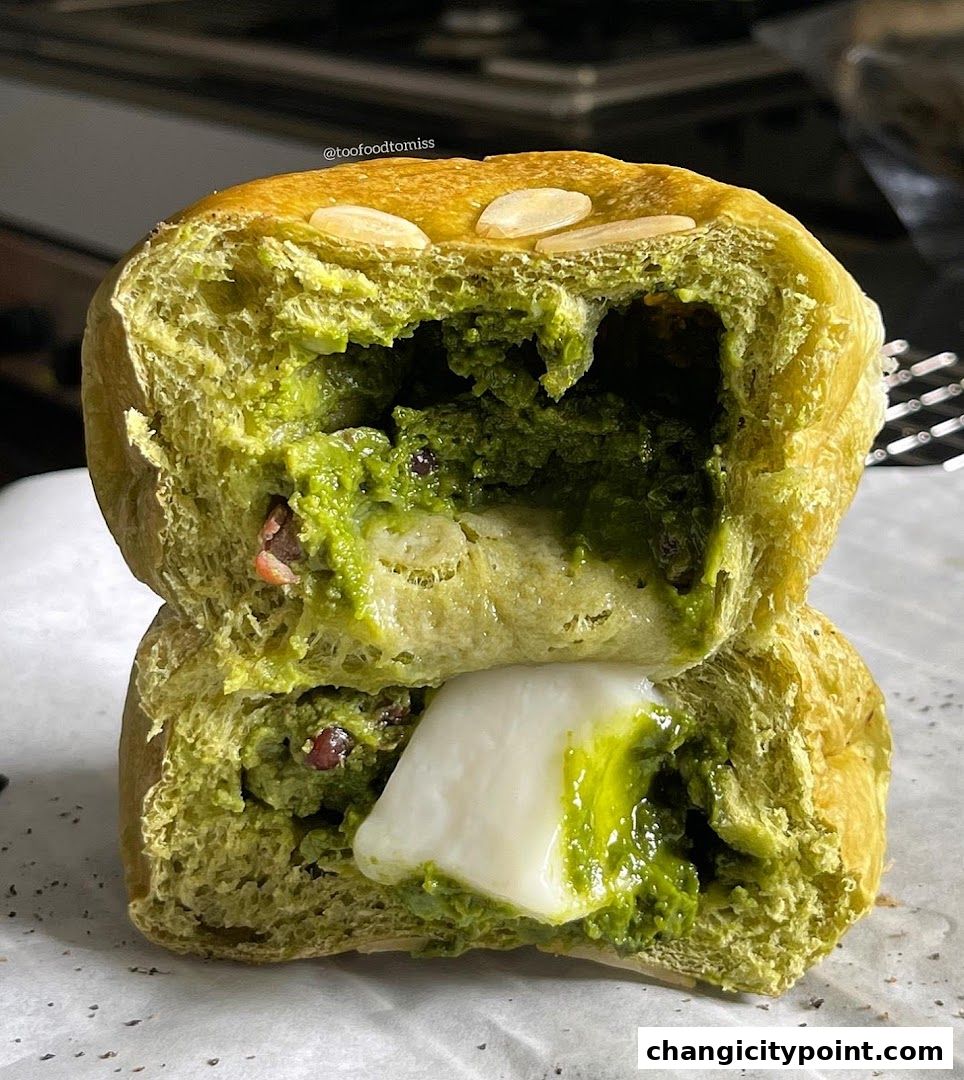 A close-up of a matcha-filled bun, cut in half, revealing creamy filling and red bean paste.
