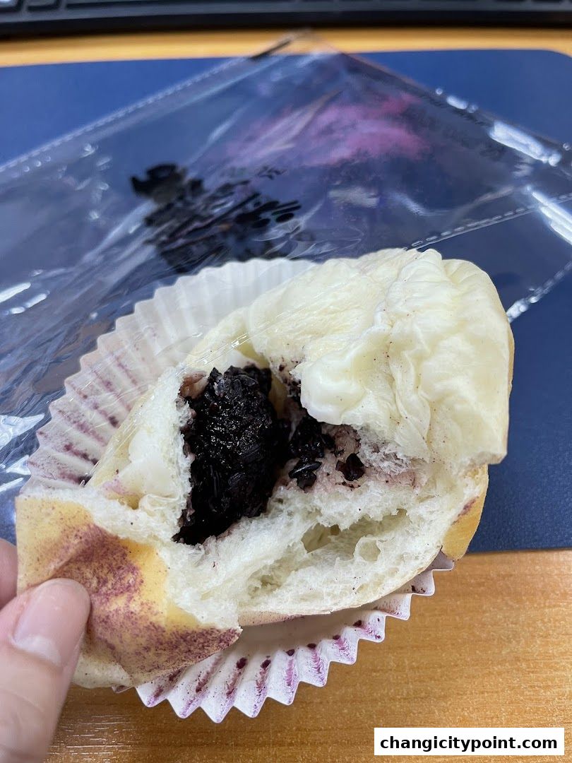 A hand holds a partially eaten pastry filled with dark fruit and cream.