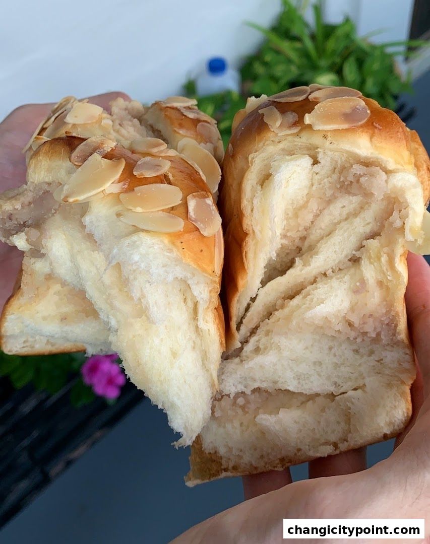 Close-up of a fluffy bread roll filled with a creamy filling and topped with sliced almonds.