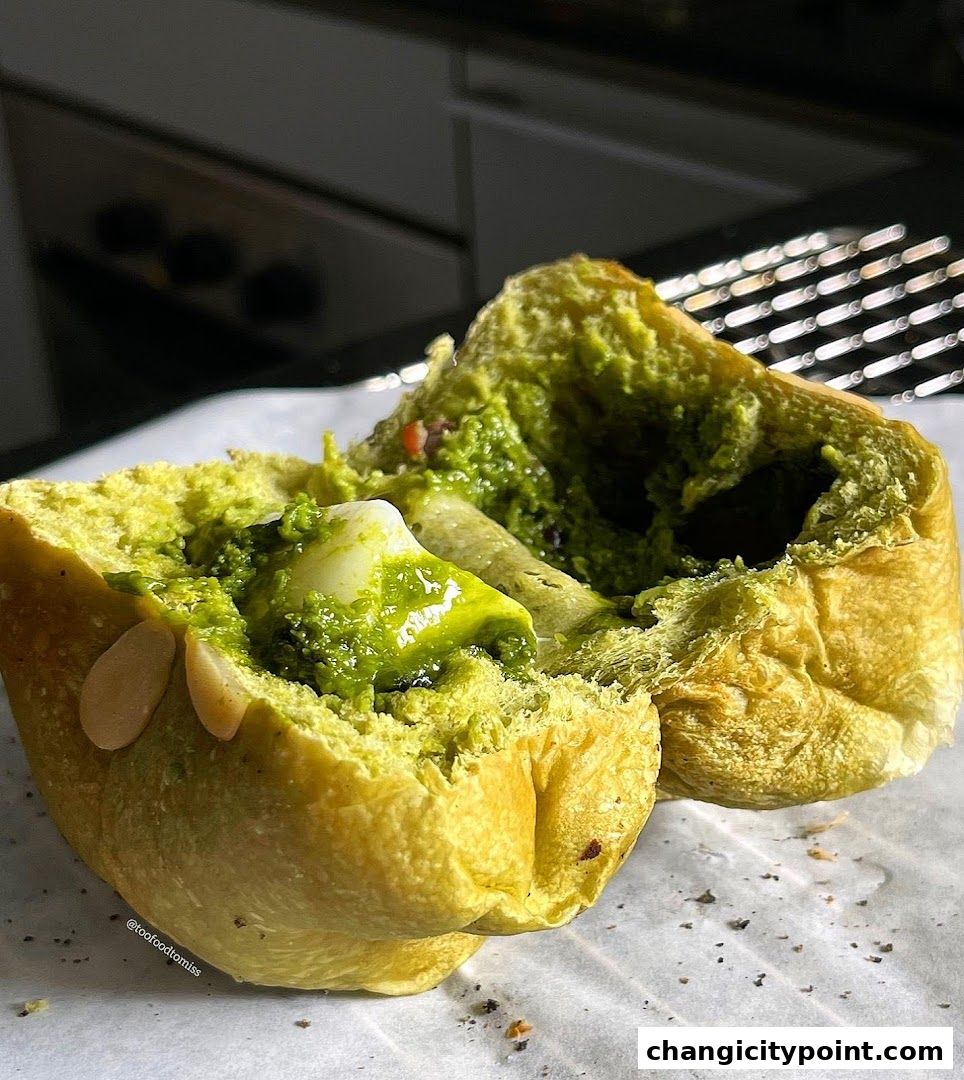 A close-up of a vibrant green pastry filled with a creamy filling and topped with nuts.
