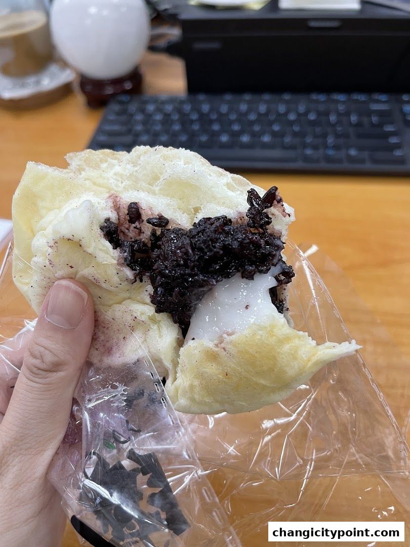 A hand holds a pastry filled with black rice and cream.