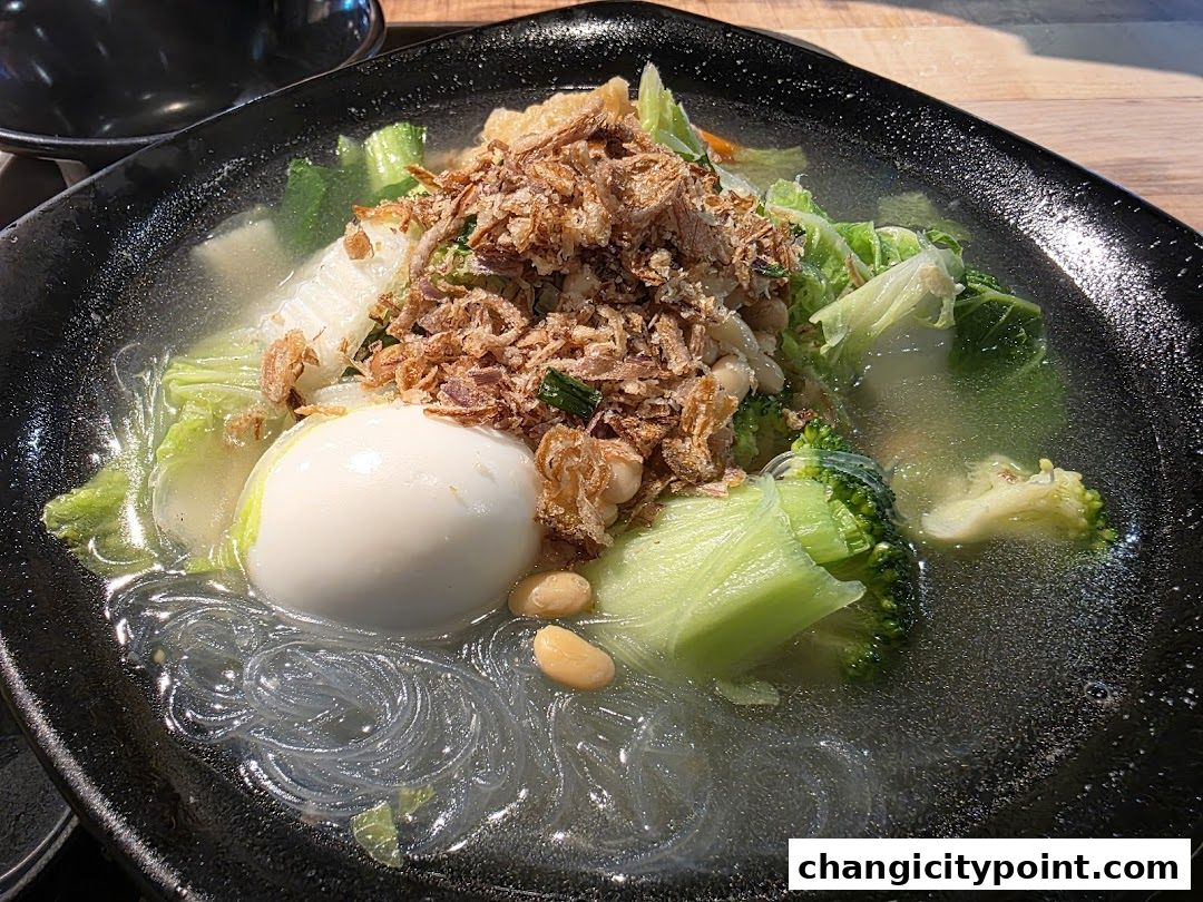A bowl of soup with vegetables, a boiled egg, noodles, and crispy toppings.