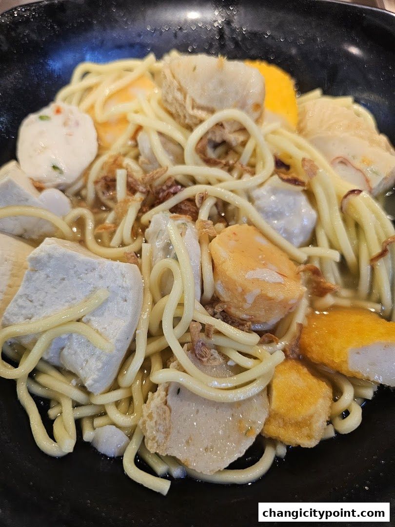 A close-up shot of a bowl of noodles with various fish cakes and tofu.