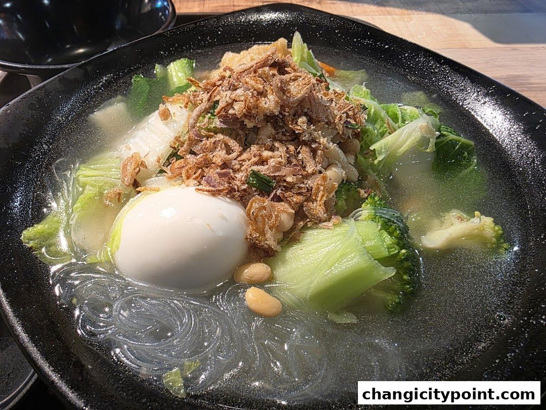 A hearty bowl of soup with vegetables, noodles, and a boiled egg, topped with crispy fried shallots.