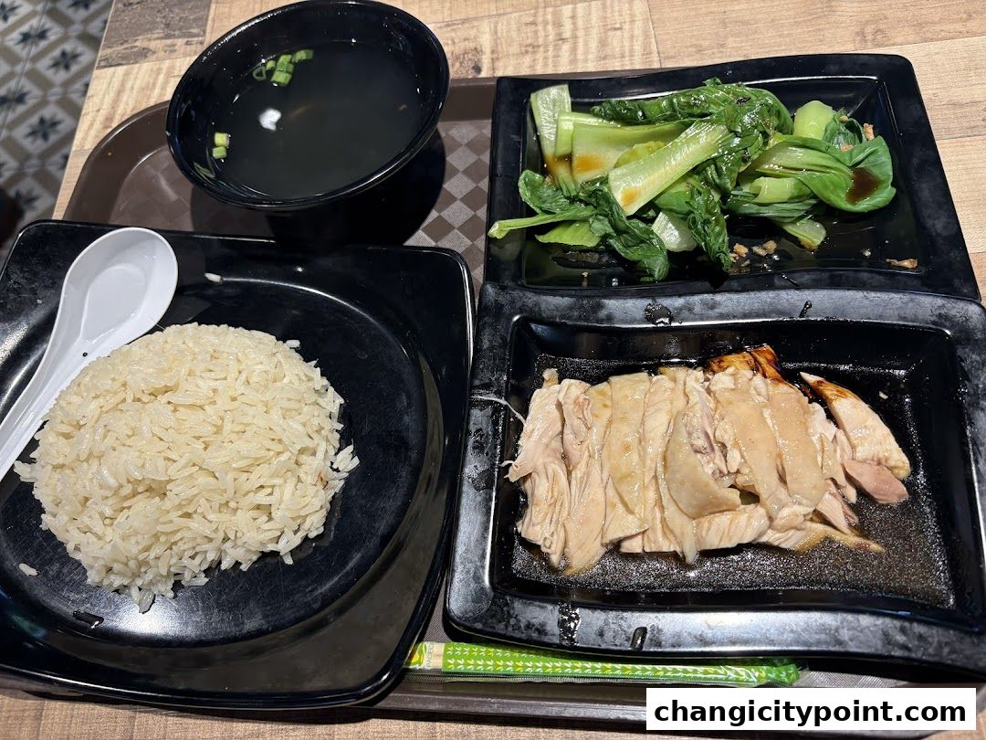 A tray of Hainanese chicken rice with soup and vegetables.