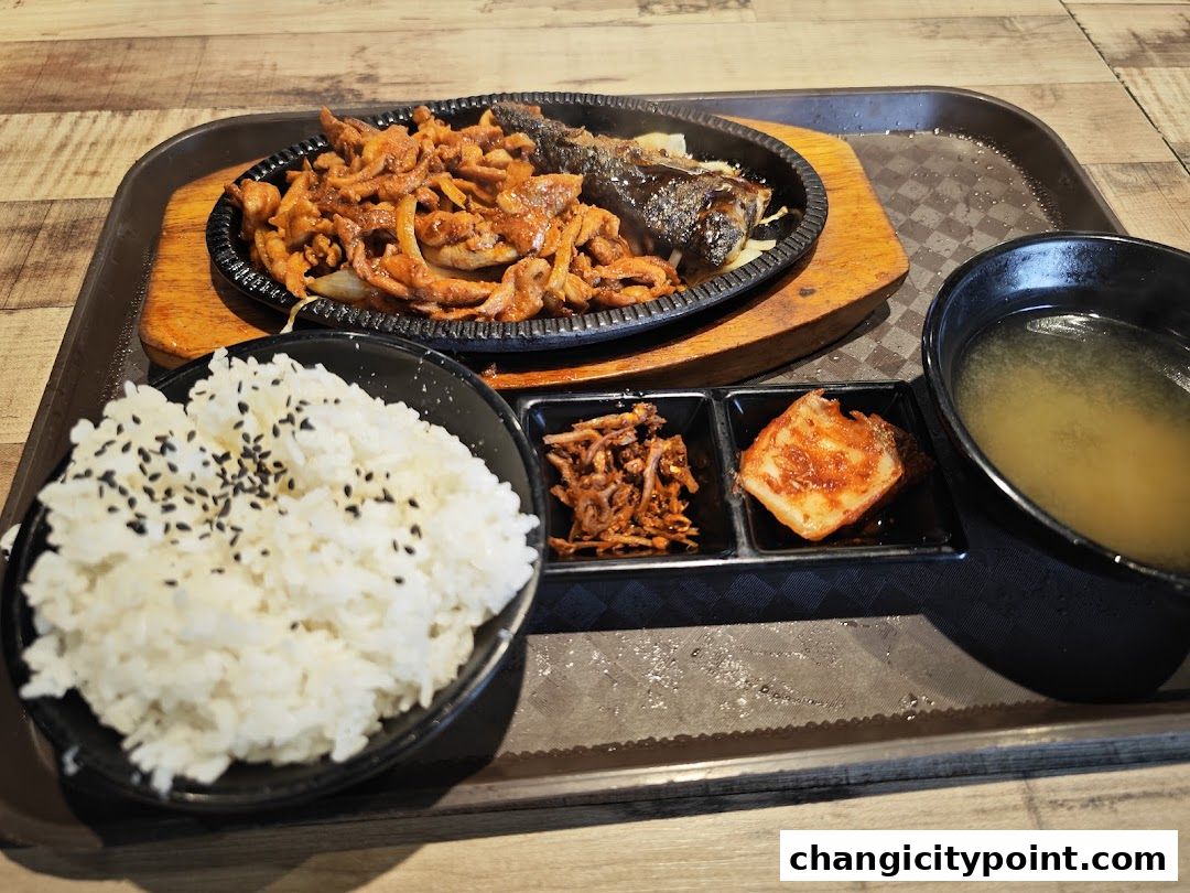 A sizzling hot plate of Korean BBQ with rice, kimchi, and soup.
