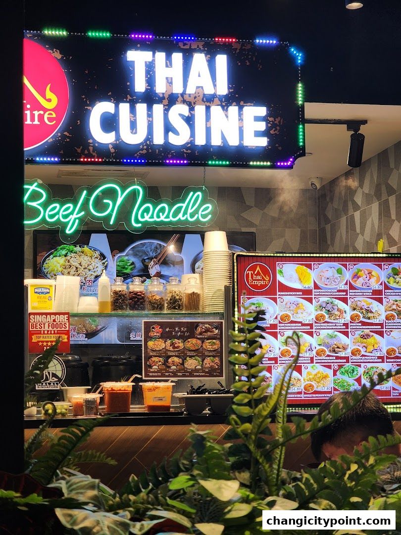 A vibrant Thai cuisine shop front with neon signs and a display of menu items.