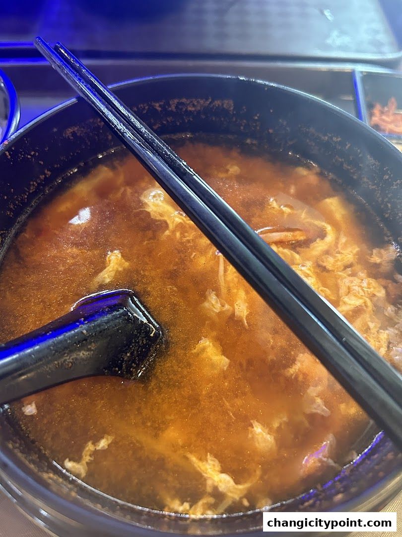 A close-up shot of a steaming bowl of soup with chopsticks and a spoon.