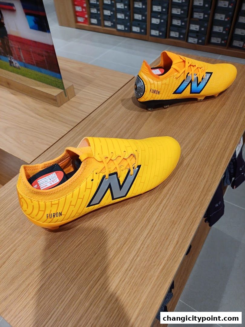 Bright yellow New Balance soccer cleats displayed on a wooden shelf in a retail store.