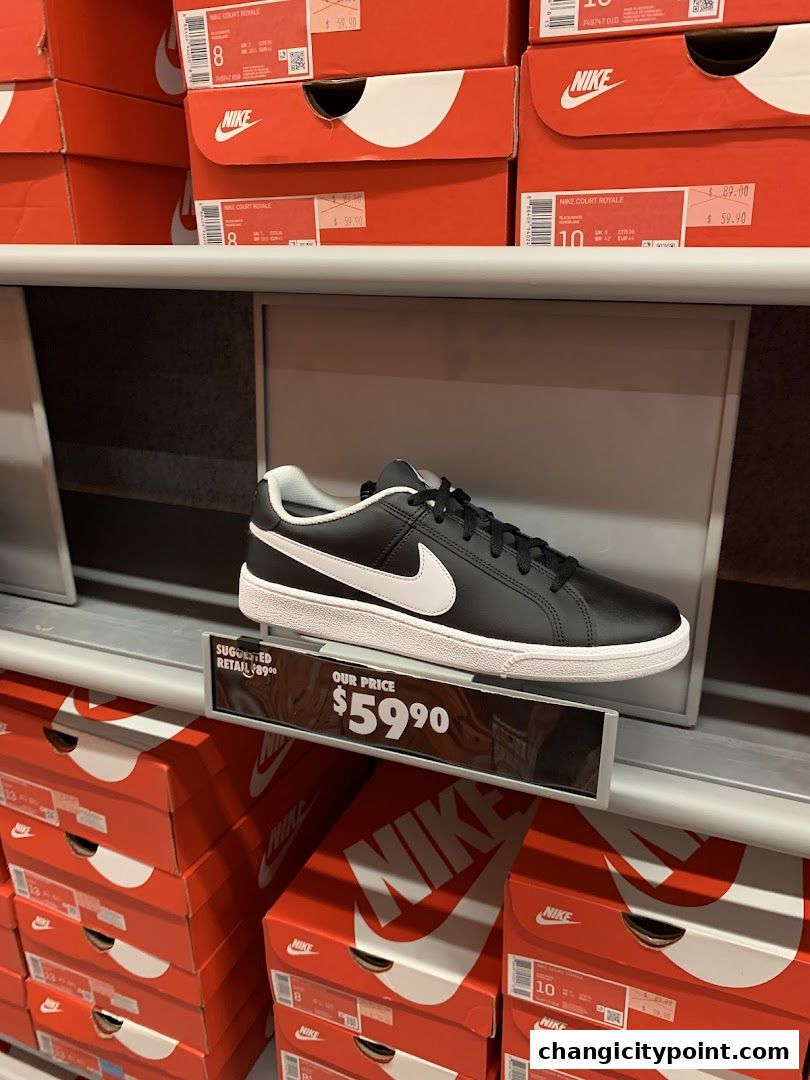A black Nike sneaker displayed on a shelf with stacked Nike shoe boxes.