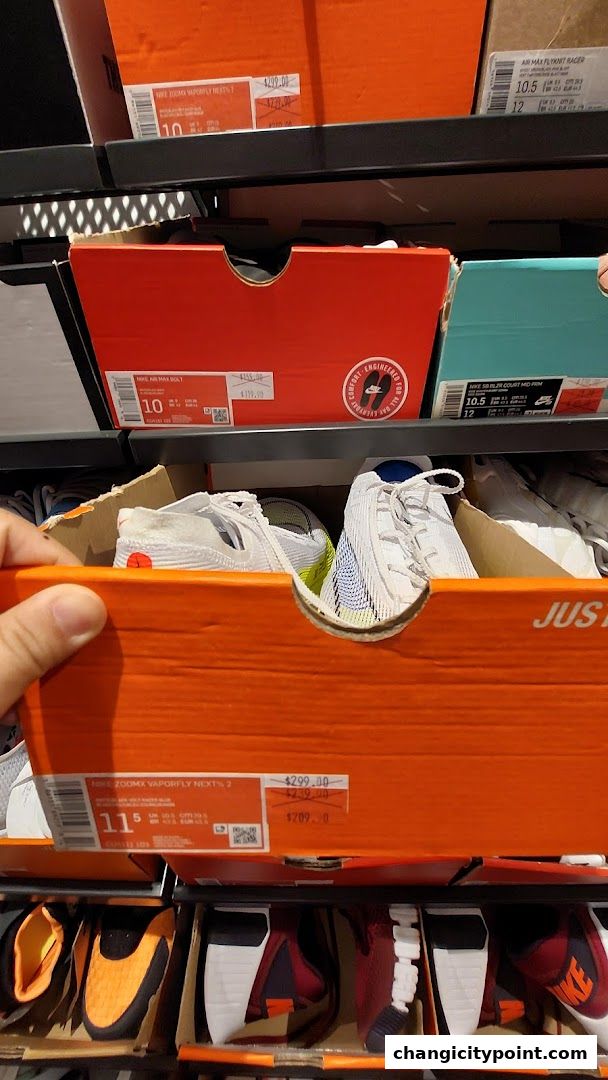 A hand reaches into an open Nike shoe box revealing running shoes on shelves.