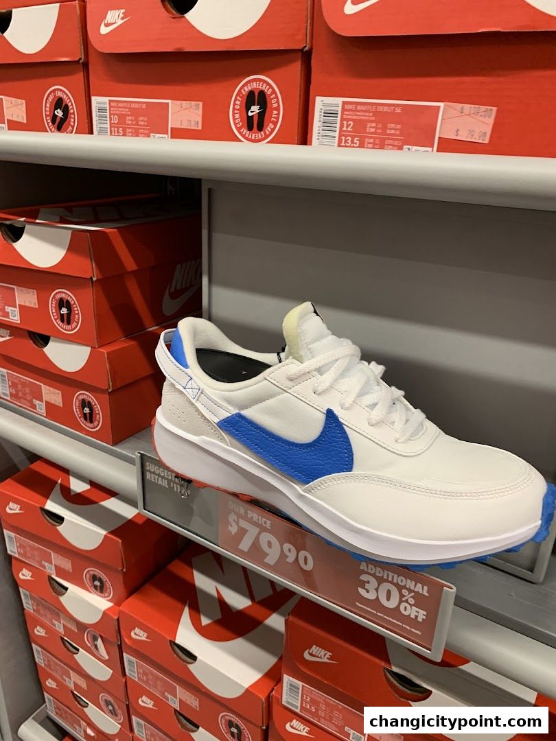 A white Nike sneaker with blue accents displayed on a shelf with Nike shoe boxes.