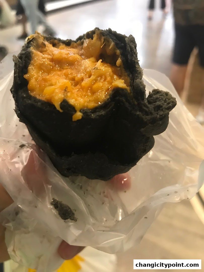 A close-up of a black charcoal bun filled with savory orange filling.