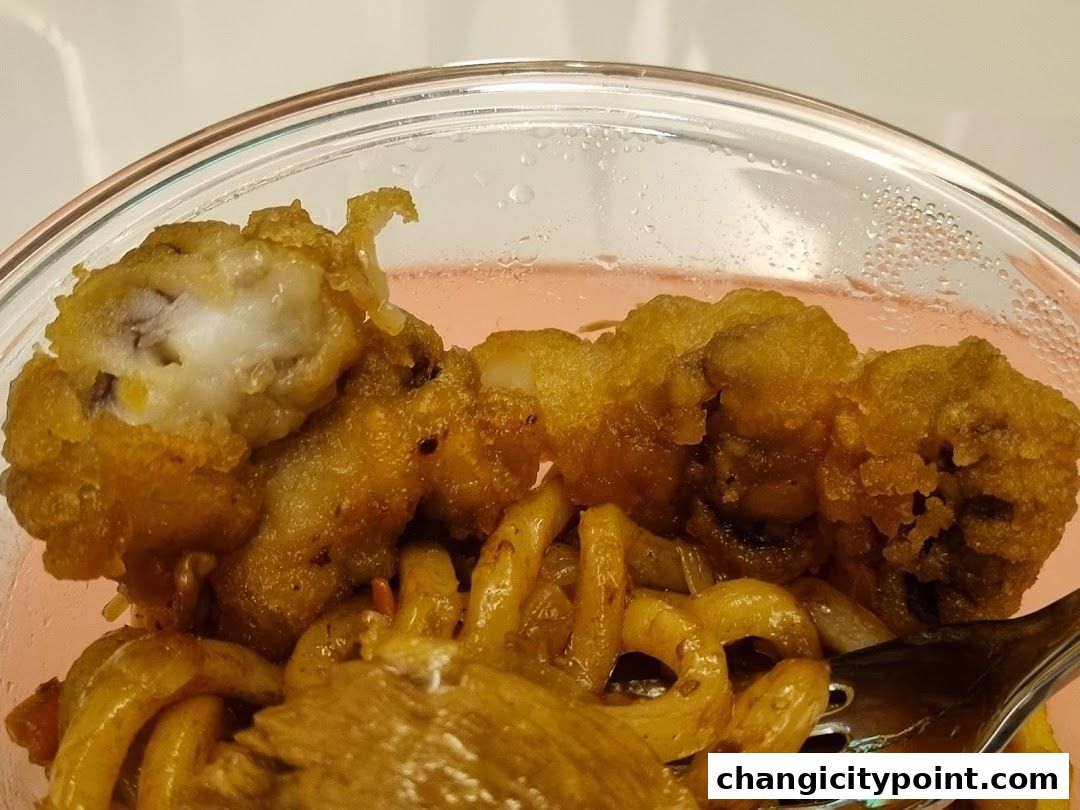Close-up of crispy fried fish pieces with noodles in a clear container.