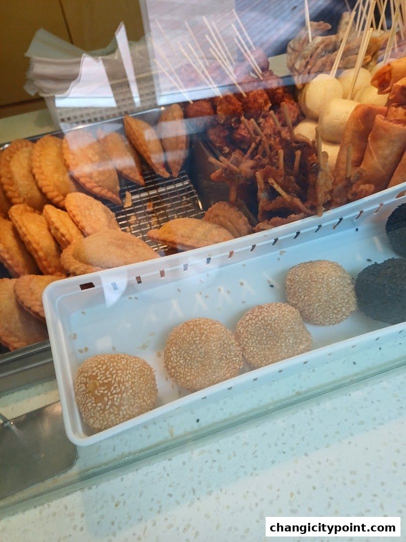 A display of various fried snacks and pastries, including curry puffs and sesame balls.