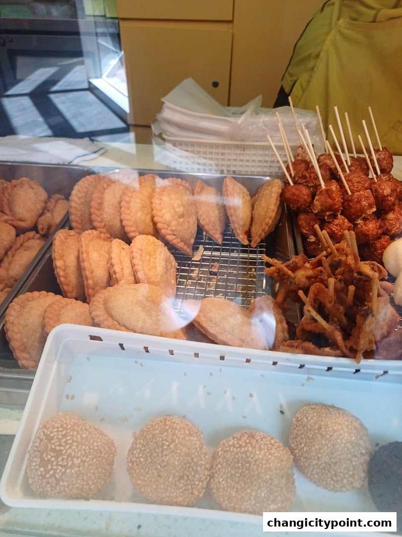 A display of various fried snacks, including curry puffs, skewers, and sesame balls.