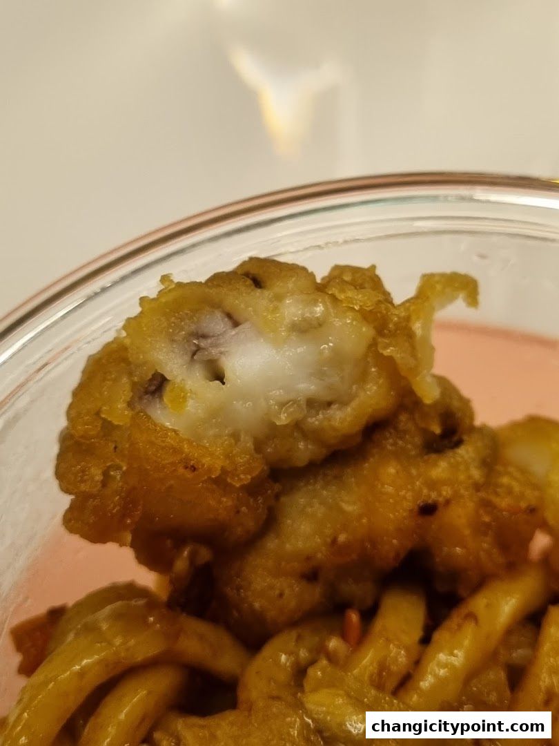Close-up of crispy fried fish pieces with noodles in a container.