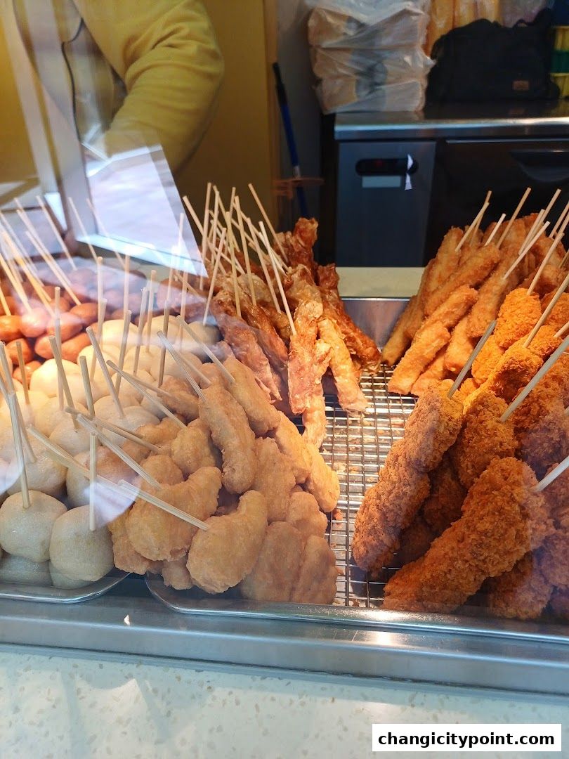 A display of various fried snacks on sticks, including fish balls, chicken nuggets, and sausages.