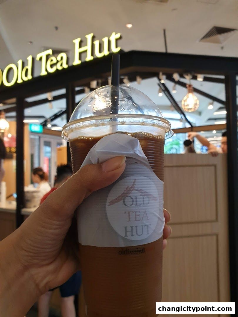 A hand holds a refreshing iced tea from Old Tea Hut with the shop's logo visible.