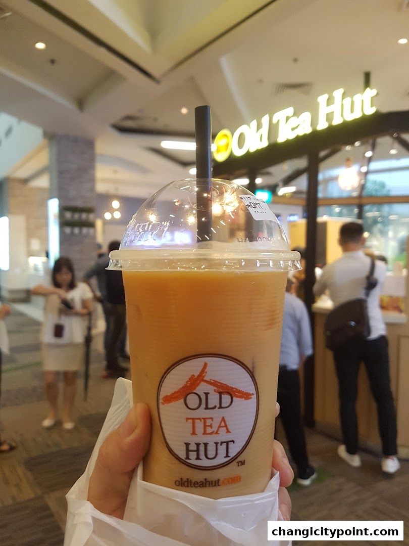A hand holds a takeaway cup of iced milk tea from Old Tea Hut.