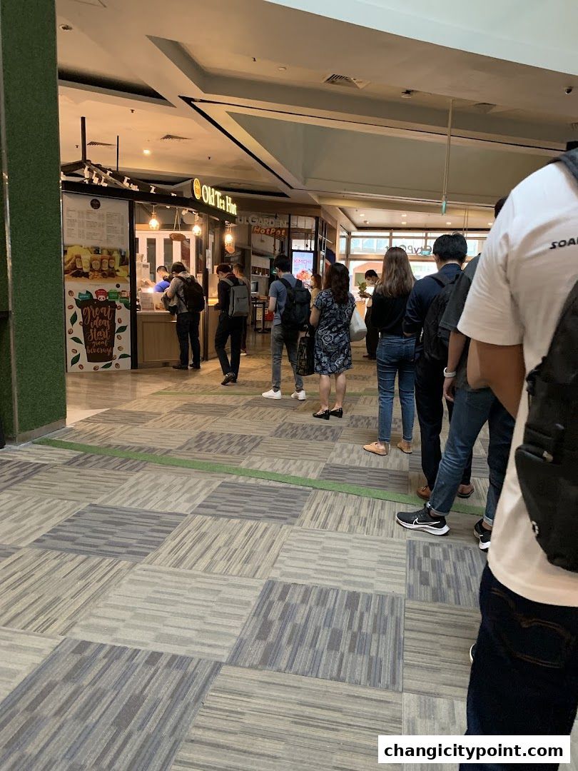 People queuing at the Old Tea Hut shop in a mall, with a menu board visible.
