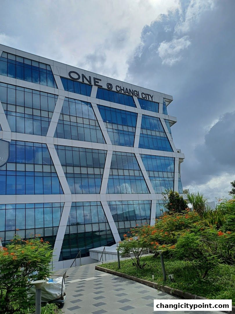 Modern building with geometric facade and lush greenery under a cloudy sky.