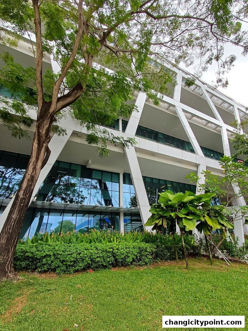 Modern building with glass facade and lush greenery in front.