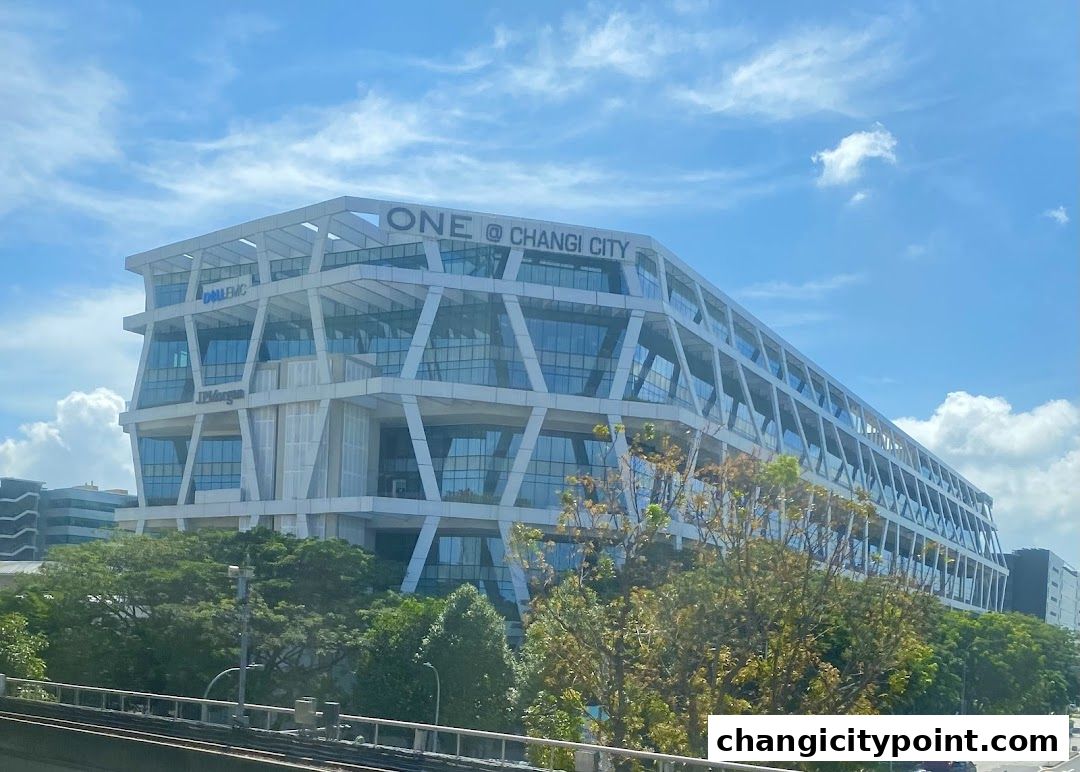 A modern office building with a distinctive geometric facade under a cloudy blue sky.