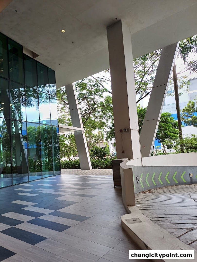 Modern architectural walkway with glass facade and outdoor greenery.