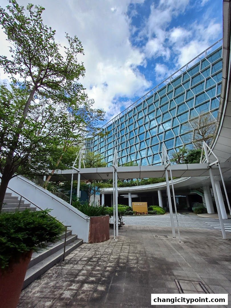 Modern building with geometric facade and outdoor walkway with stairs and greenery.