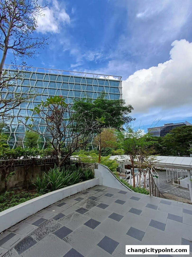 Modern building with geometric facade surrounded by lush greenery and blue sky.