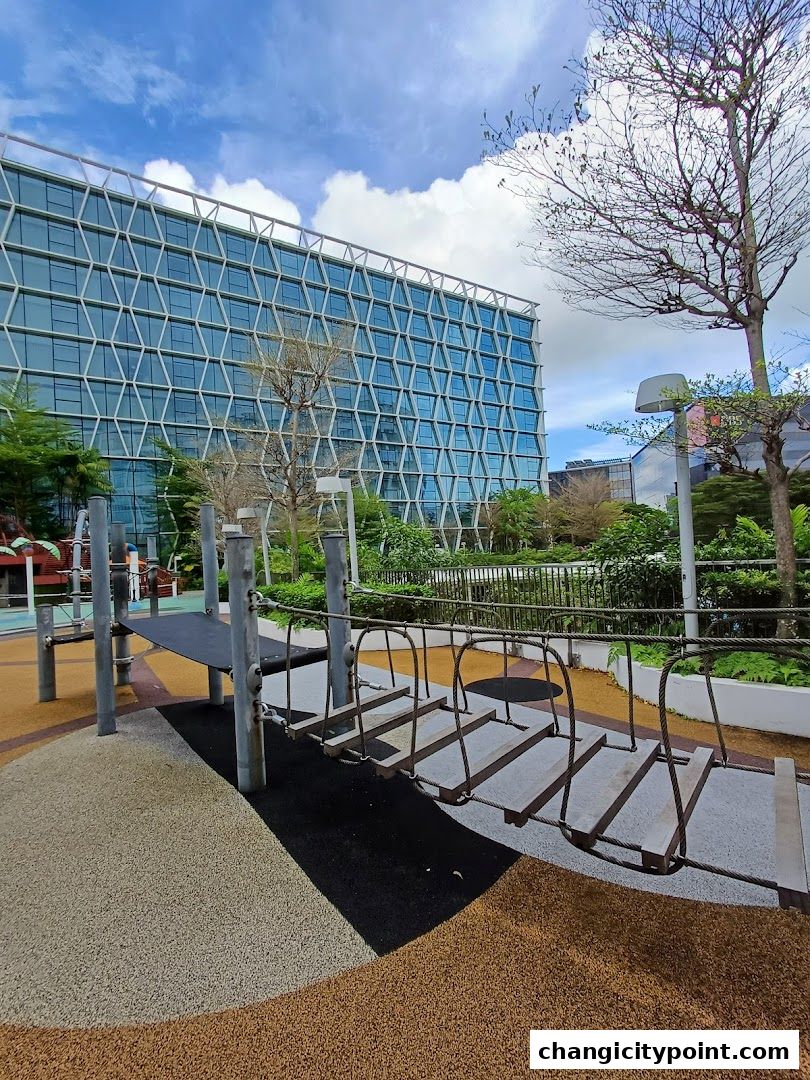 A modern building overlooks a colorful playground with a rope bridge.