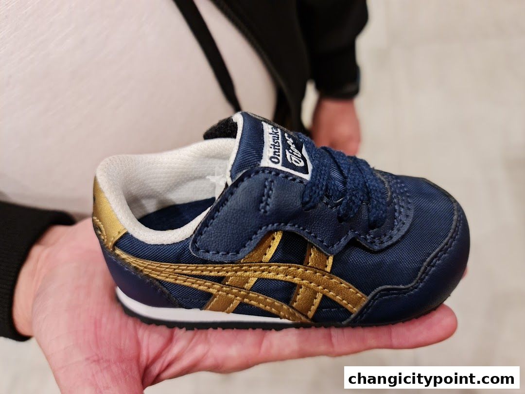 A hand holds a small navy blue Onitsuka Tiger sneaker with gold accents.