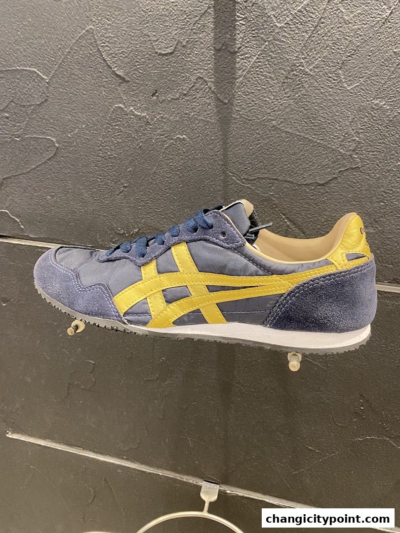 A close-up of a blue and yellow Onitsuka Tiger sneaker displayed on a shelf.
