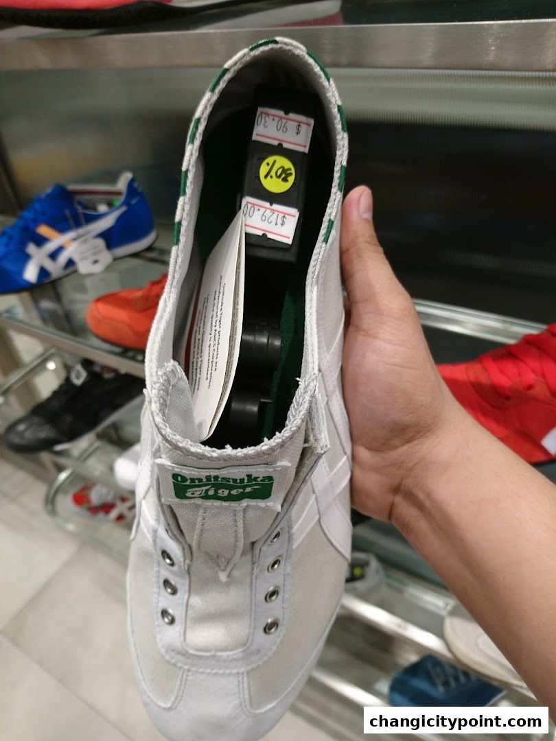 A hand holds a white Onitsuka Tiger shoe with price tags inside.