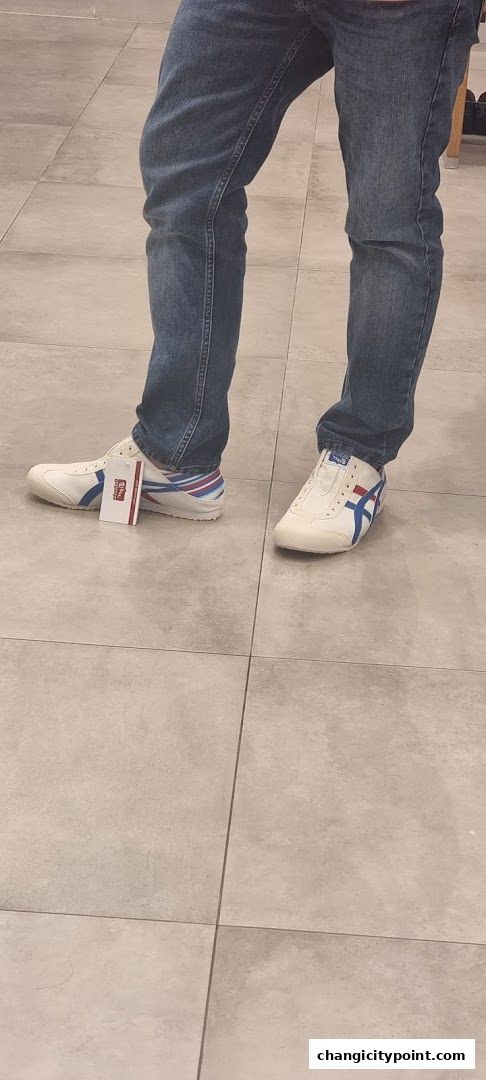 A person wearing blue jeans and white Onitsuka Tiger sneakers with blue and red stripes.